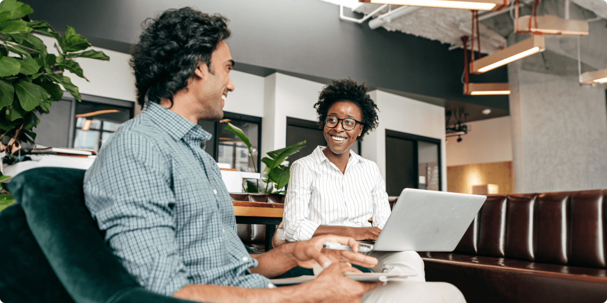 Deux personnes sourient dans un salon de bureau décontracté, tout en travaillant.